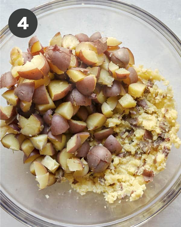 Mashed potatoes in a glass bowl with chopped potatoes.