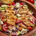 Greek salad recipe in a bowl with red wine vinaigrette being poured over it.