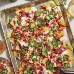 Chipotle chicken sheet pan nachos with plates on the side.