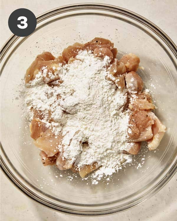 Chicken thighs in a glass bowl with cornstarch.