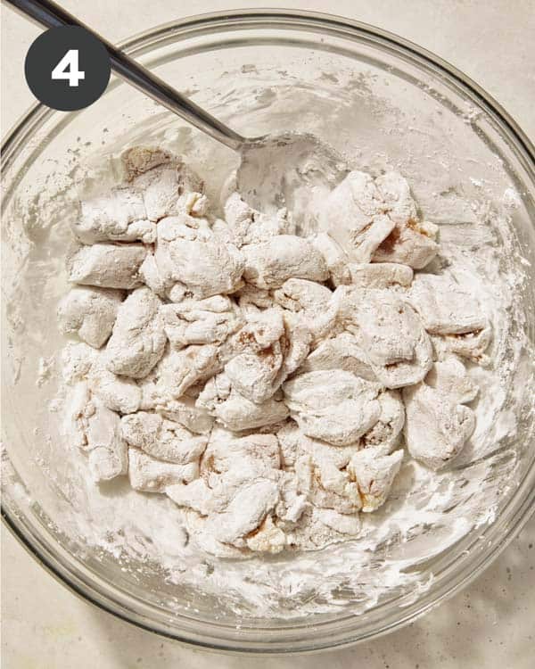 Chicken thighs tossed in cornstarch in a glass bowl.