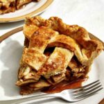 A slice of apple pie on a plate with a fork next to it.