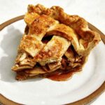 A slice of apple pie on a plate with a fork next to it.