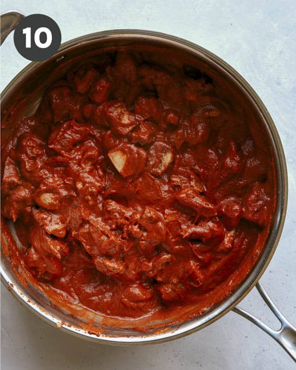 Butter chicken sauce and chicken in a skillet simmering. 