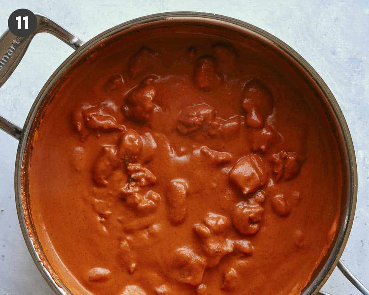 Butter chicken with cream stirred in simmering in a skillet. 