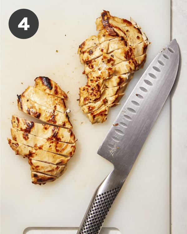 Slicing chicken on a cutting board for a greek salad. 