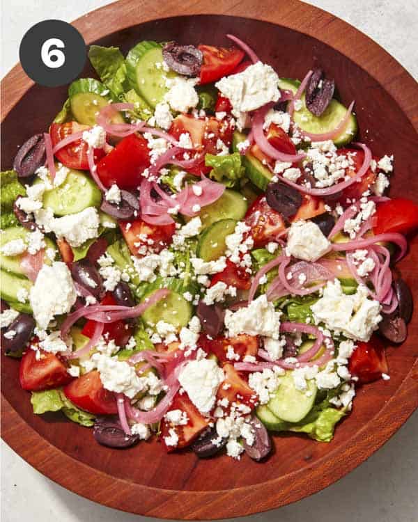 A greek salad being tossed together in a wood bowl.