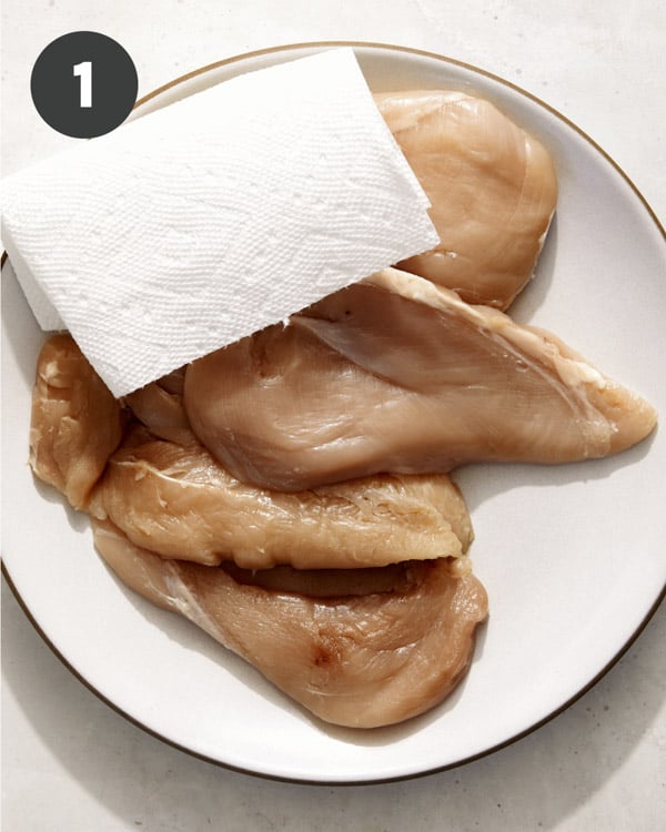 Chicken breasts being pat dry on a plate.