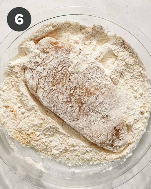 A chicken breast being dredges in a flour mixture.