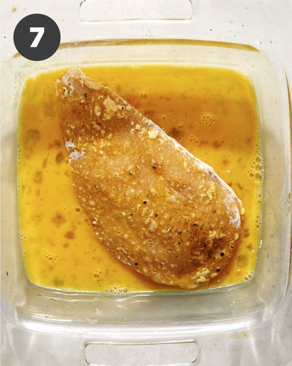 A chicken breast in an egg wash to make a hot honey chicken sandwich.