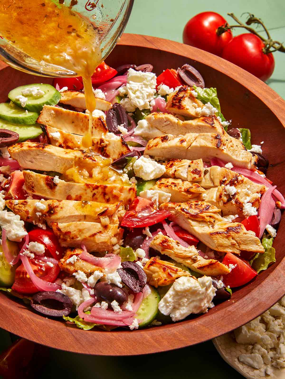 Greek salad recipe in a bowl with red wine vinaigrette being poured over it. 