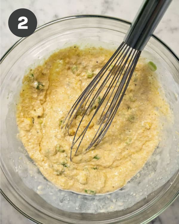 Hush Puppies batter in a glass bowl shot overhead with a whisk in the batter.