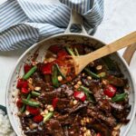 Kung pao beef in a skillet with rice on the side.