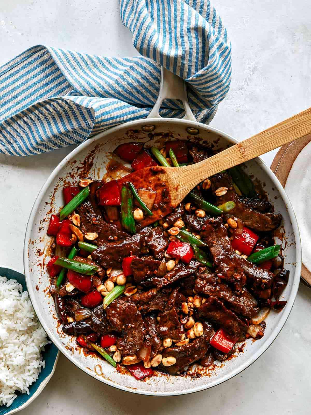 Kung pao beef in a skillet with rice on the side. 