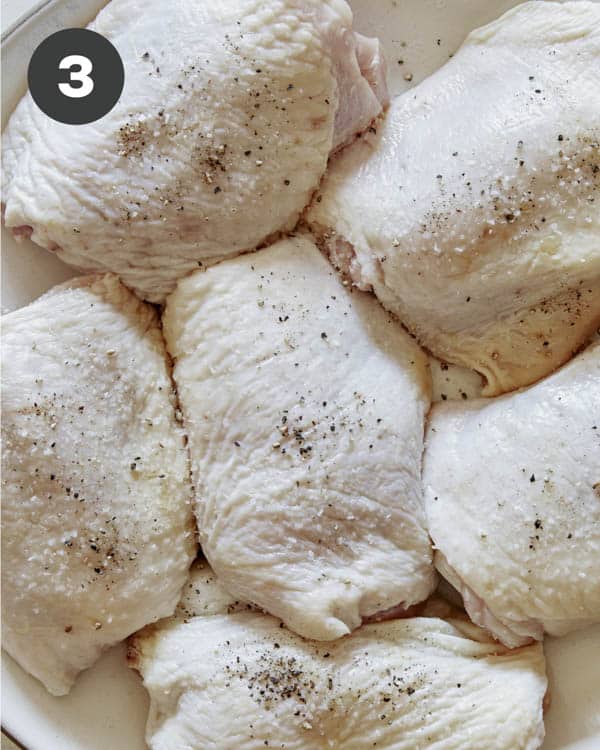 Seasoned raw chicken thighs on a plate with salt and pepper.