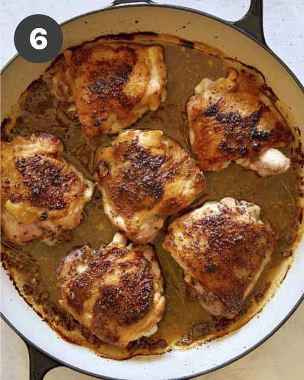 Baked chicken thighs with sauce in a skillet.