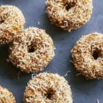 Baked pumpkin donuts on a surface with coconut.