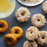 Baked pumpkin donuts being glazed and covered in coconut.