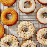 Baked pumpkin donuts being glazed and covered in coconut.