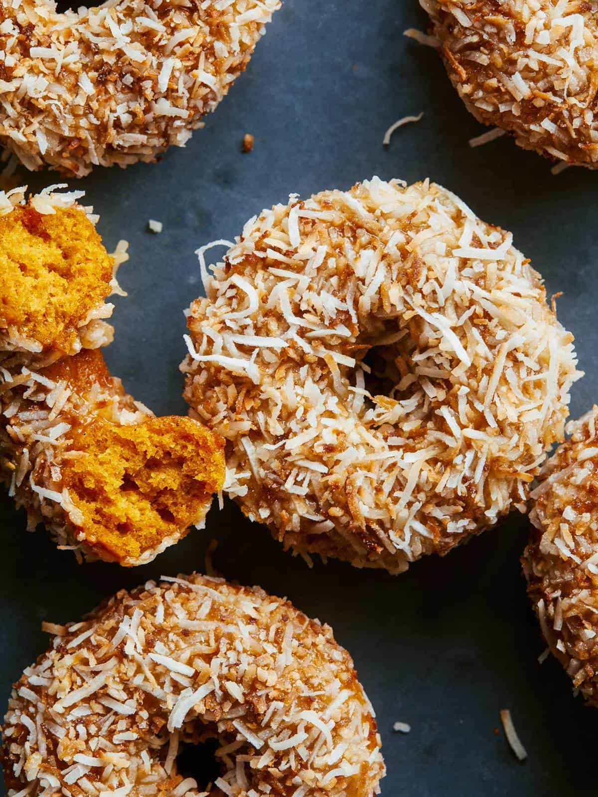 A close up of baked pumpkin cake doughnuts with maple glaze and toasted coconut.