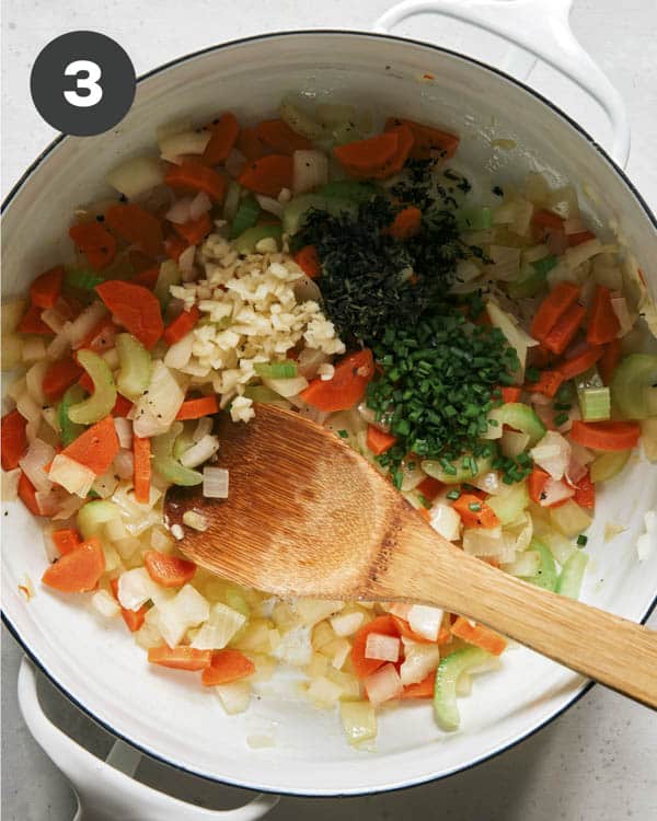 Vegetables cooking in a stock pot with garlic and herbs.