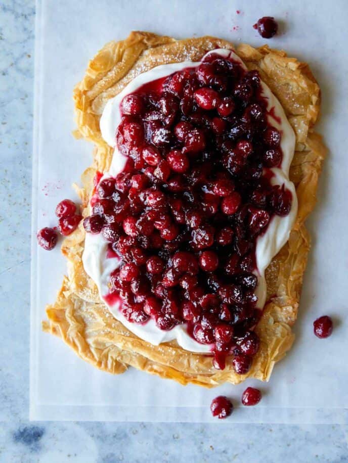 A crostata topped with yogurt filling and cranberries with the end cut off.