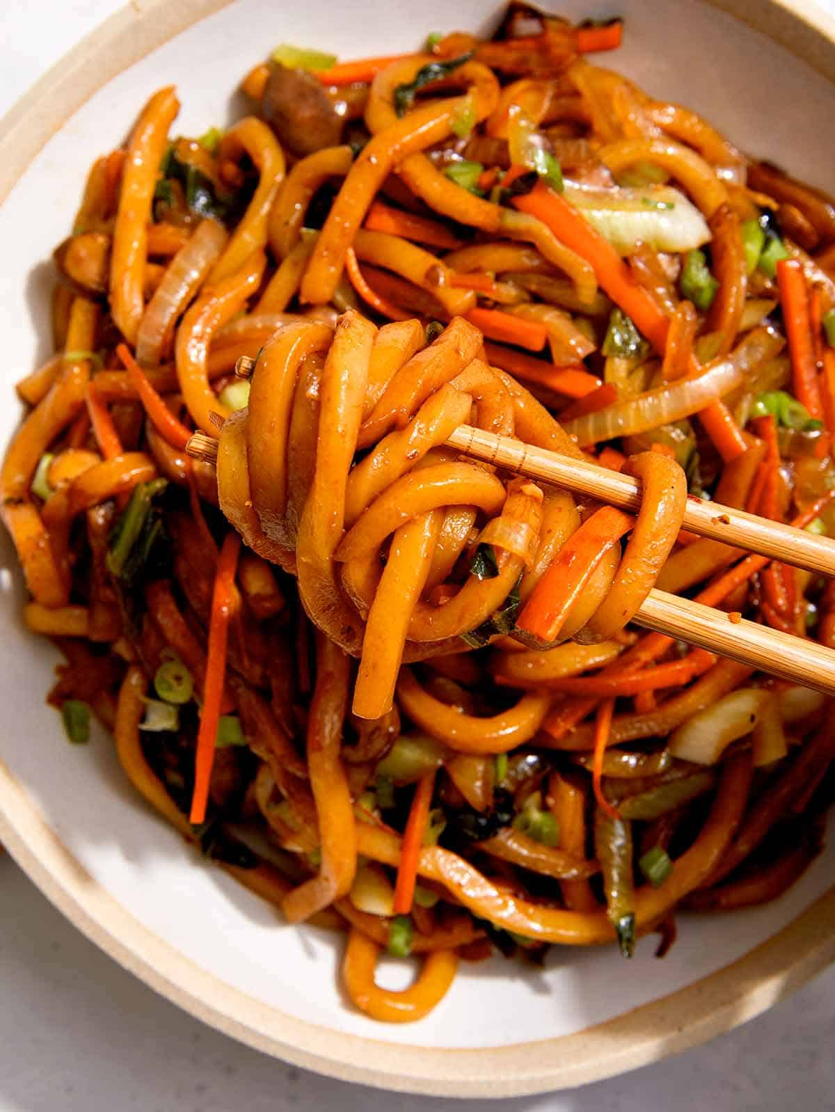 Yaki udon noodles with chop sticks taking a bite. 