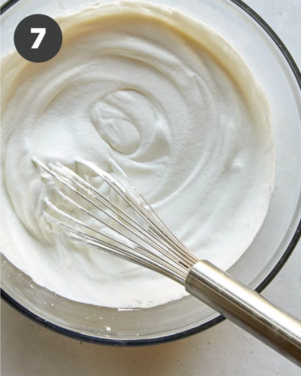 Whipped cream with a whisk in a glass bowl. 