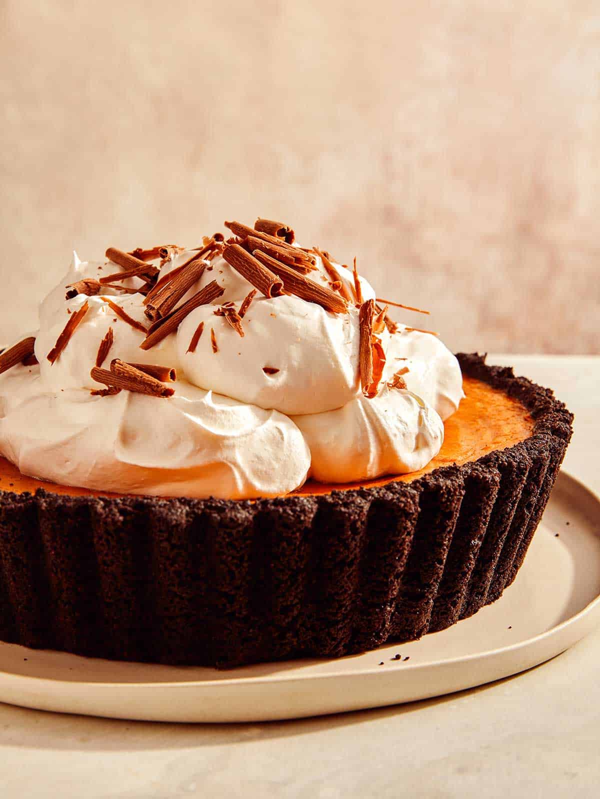 Pumpkin pie with a chocolate crust with whipped cream and chocolate shavings. 