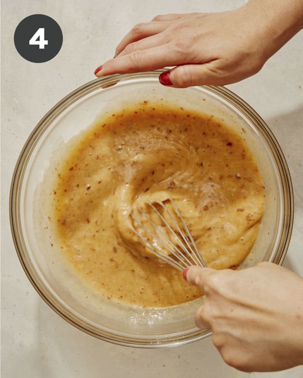 Wet mixture in a bowl being whisked together. 