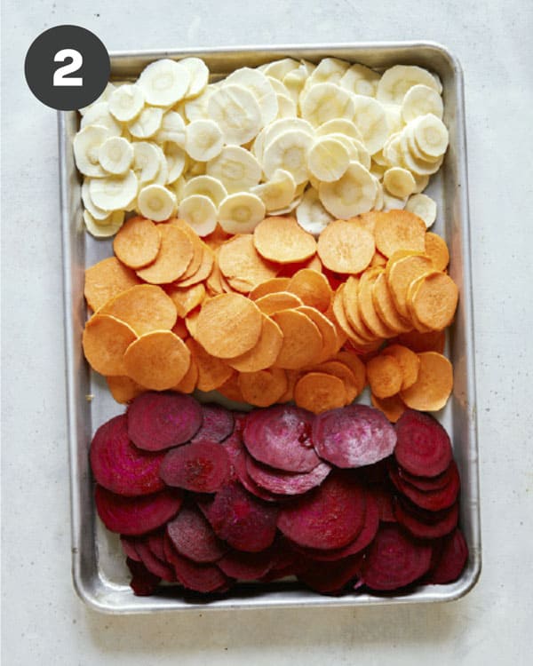 A baking sheet with sliced root vegetables on it.