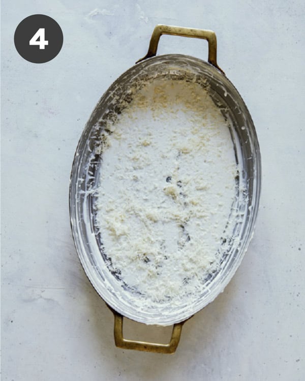 A buttered baking dish with a layer of cream, parmesan, and garlic.