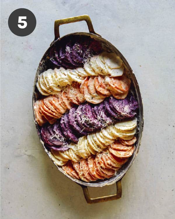 A baking dish full of sliced root vegetables to make a root vegetable gratin.