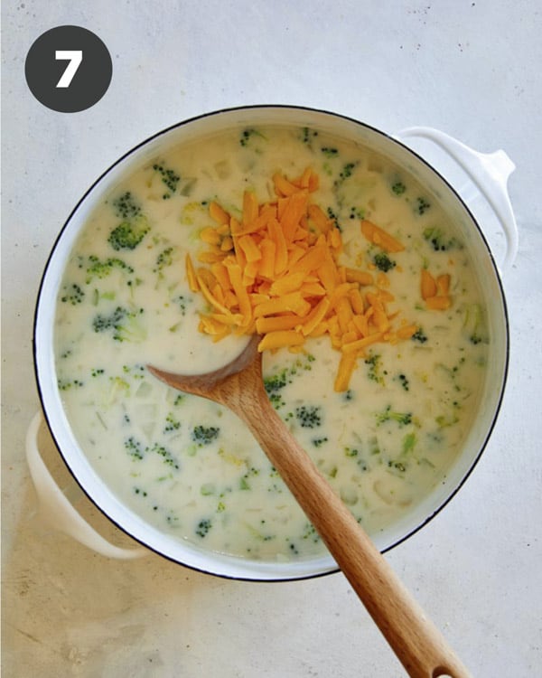 Hand fulls of cheese added into a stock pot to make broccoli cheddar soup.