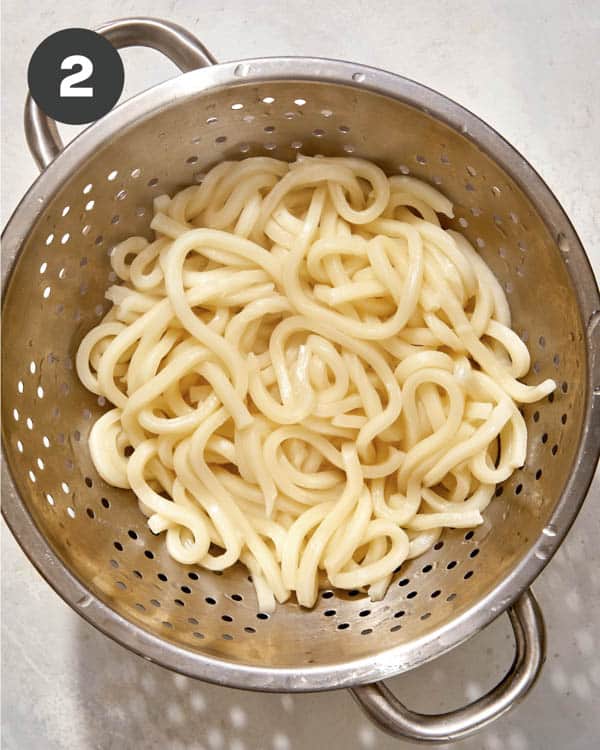 Udon noodles cooked and draining in a colander. 