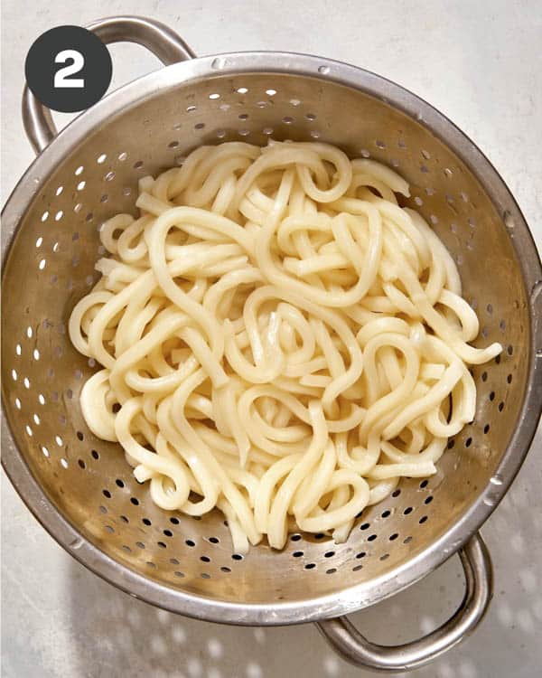 Udon noodles cooked and draining in a colander.