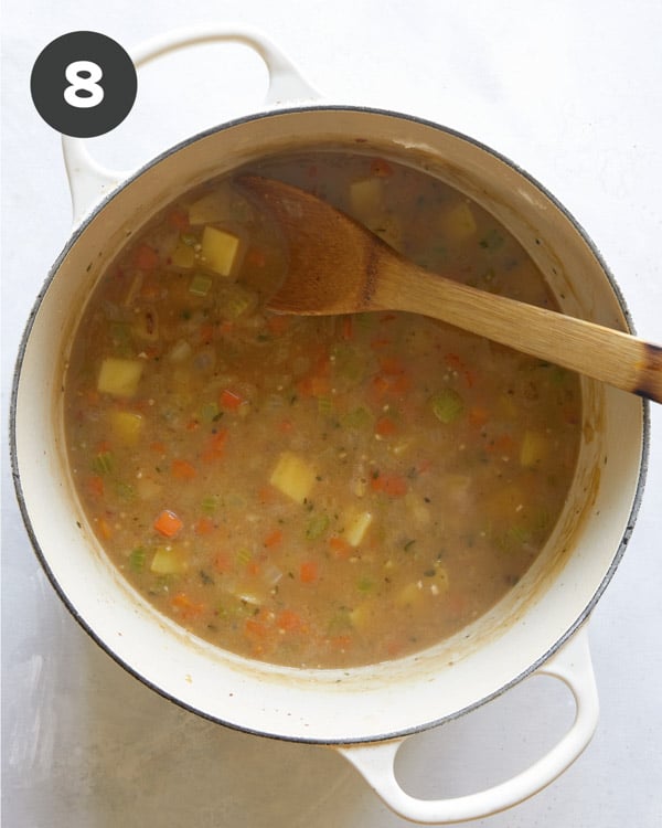 Zuppa toscana recipe simmering in a pot with a wooden spoon. 