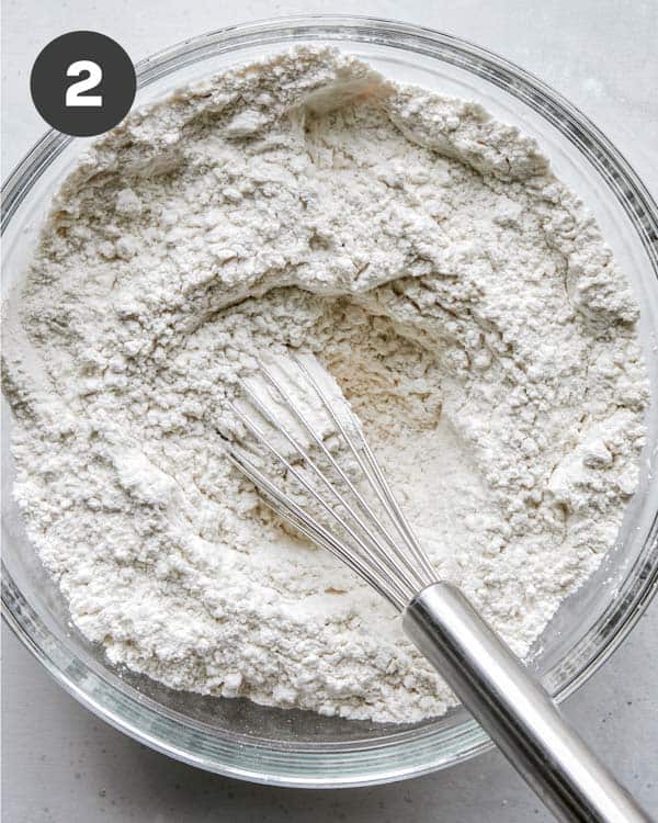 Flour combined in a glass bowl with a whisk. 