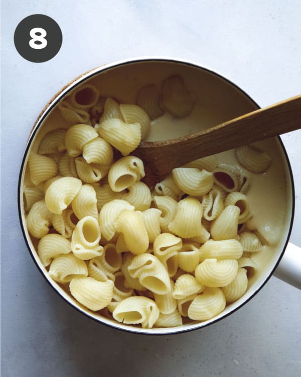 Adding pasta to a skillet with cheese sauce.