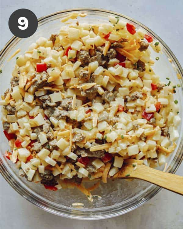 Breakfast casserole mixture in a glass bowl with a spoon in it.