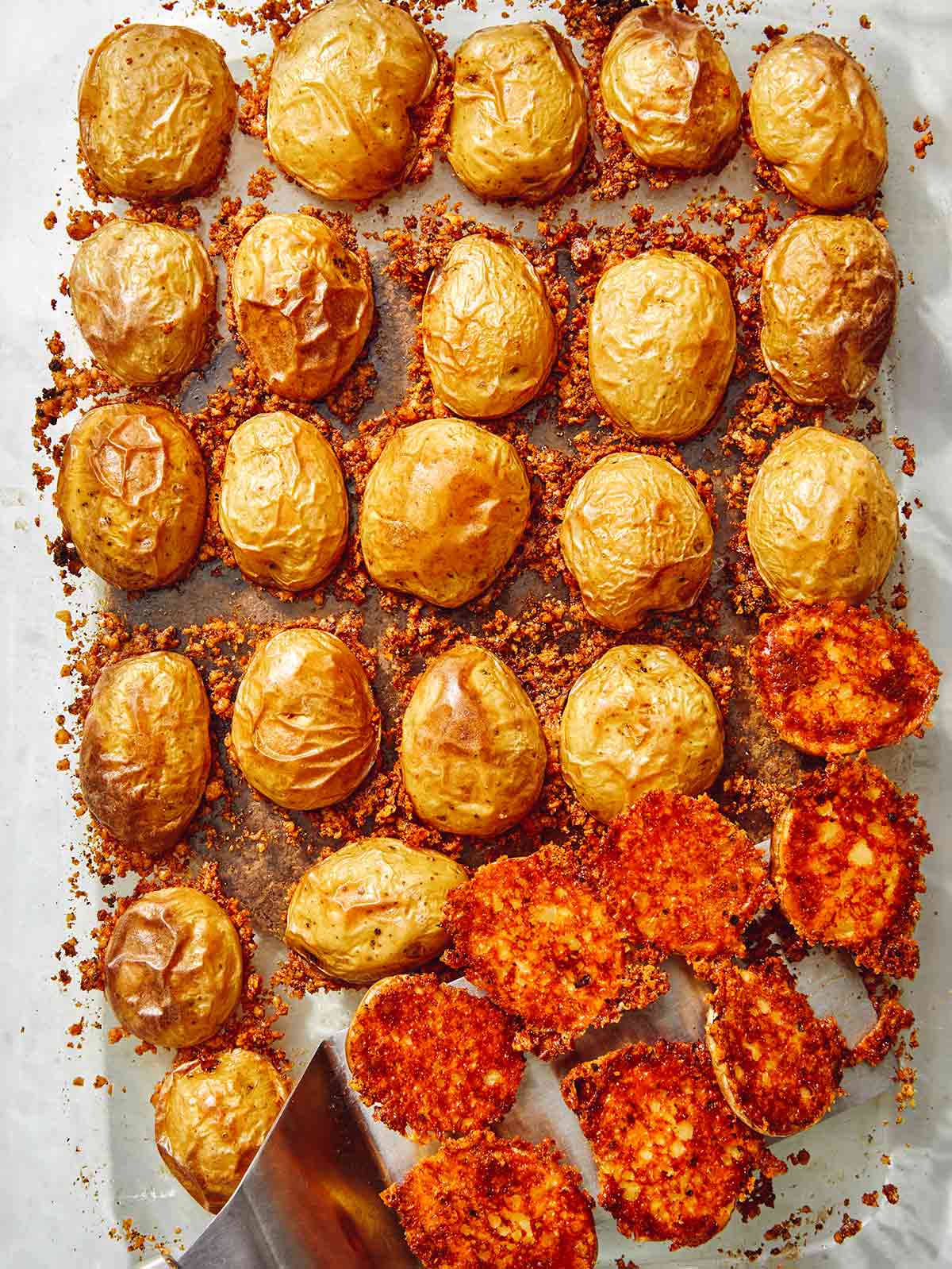 Crispy parmesan potatoes in a baking dish with a spatula.