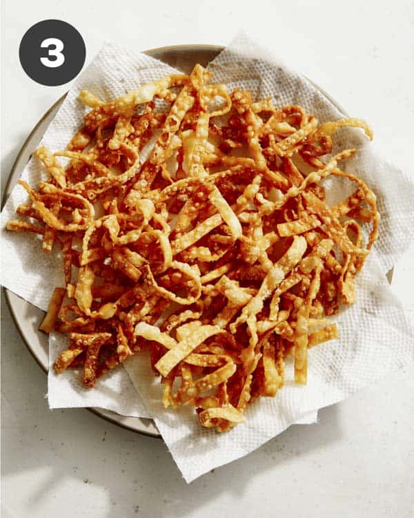 Crispy fried wontons being drained on a paper towel. 