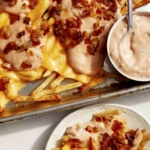 Animal style fries on a baking sheet served on plates.