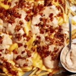 Animal style fries on a baking sheet with dressing on the side.