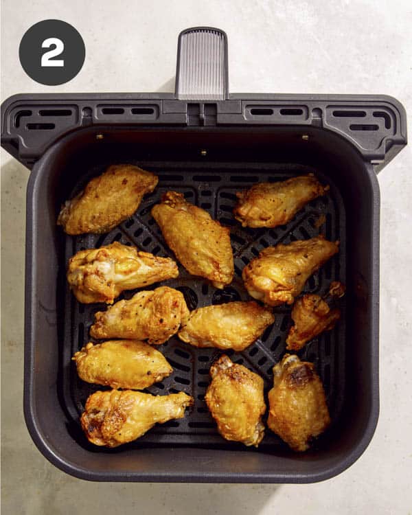 Buffalo wings in an air fryer being cooked.