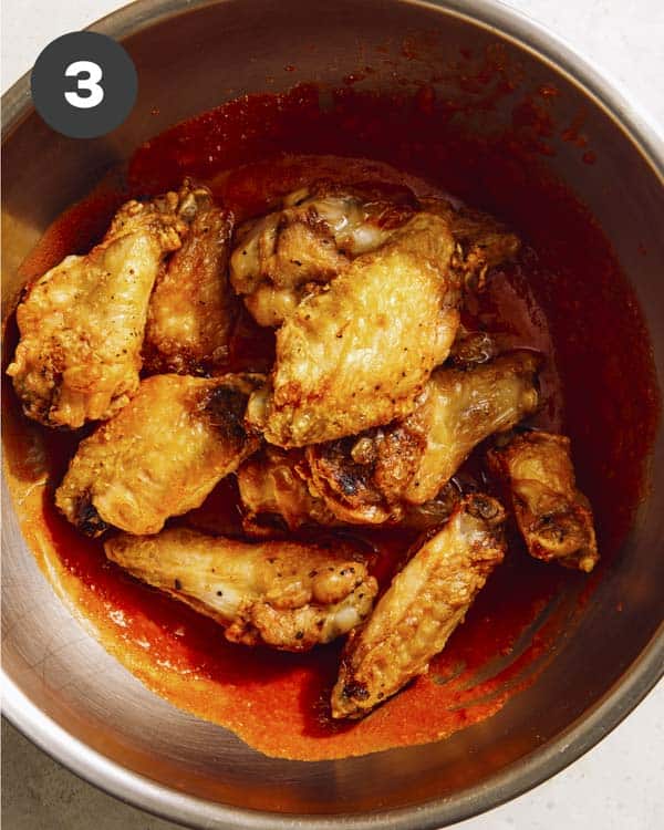 Buffalo wings being tossed in buffalo sauce.