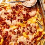 Animal style fries on a baking sheet with dressing on the side.