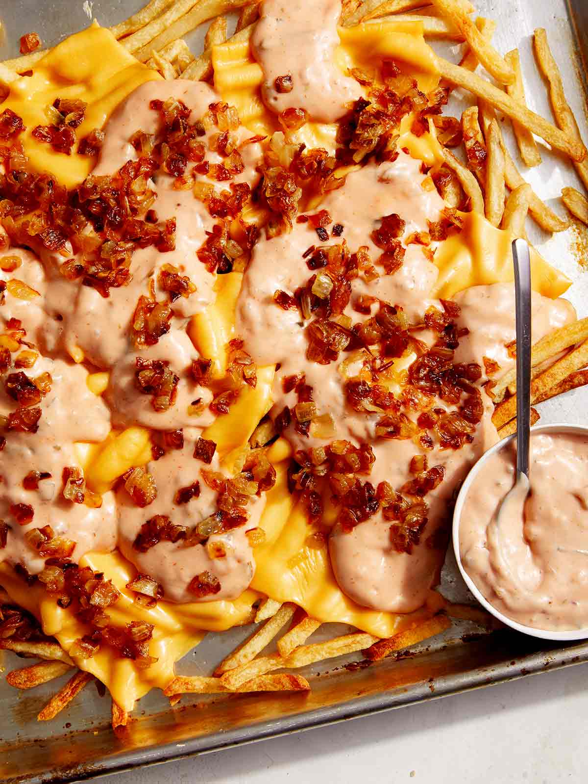 Animal style fries on a baking sheet with dressing on the side.