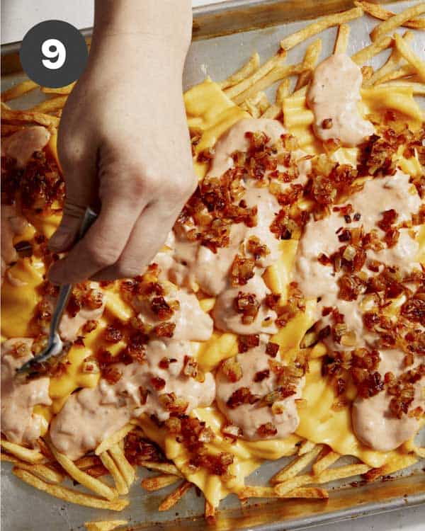 Animal style fries on a baking sheet with cheese and spread on top. 