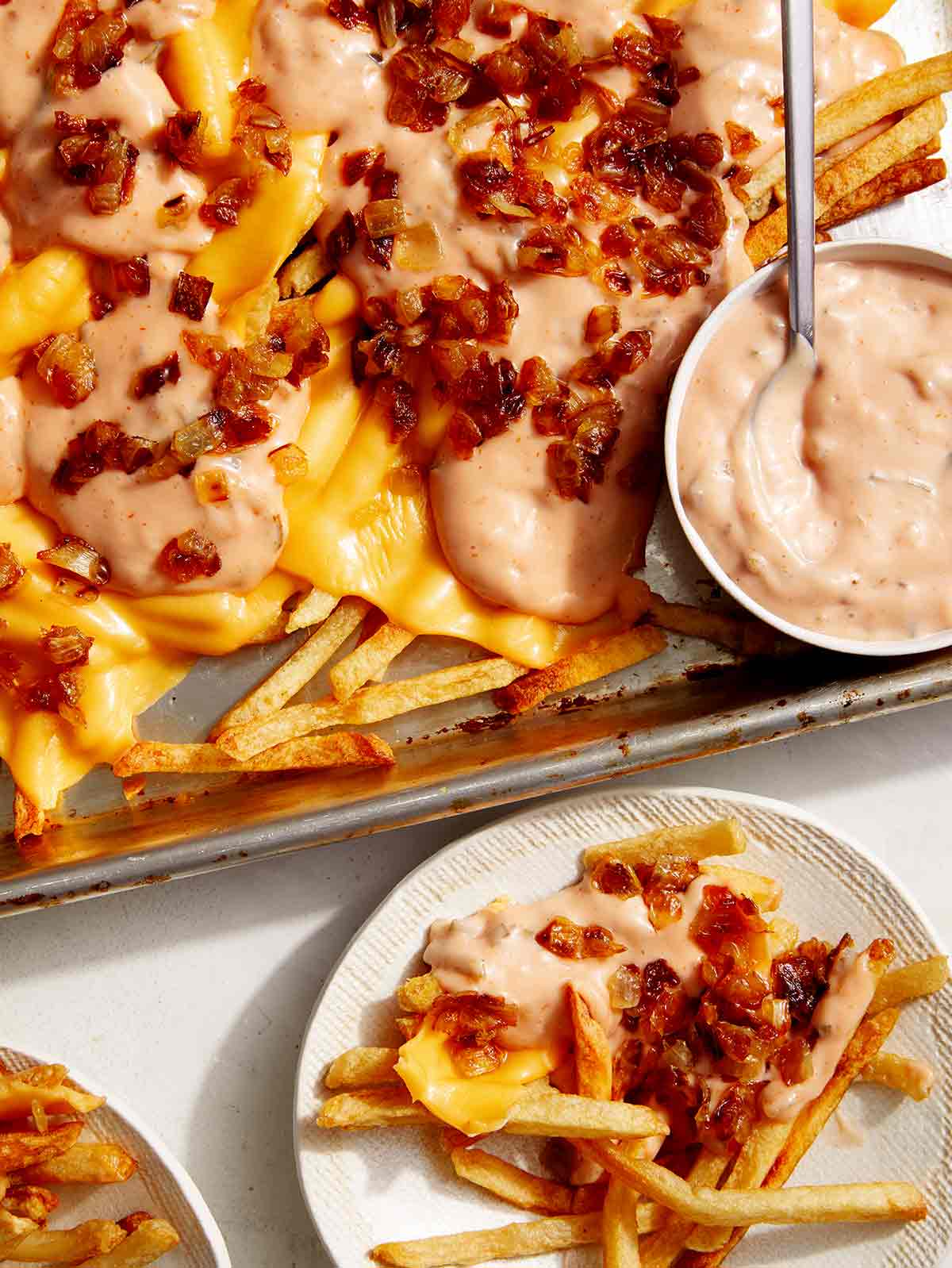 Animal style fries on a baking sheet served on plates.